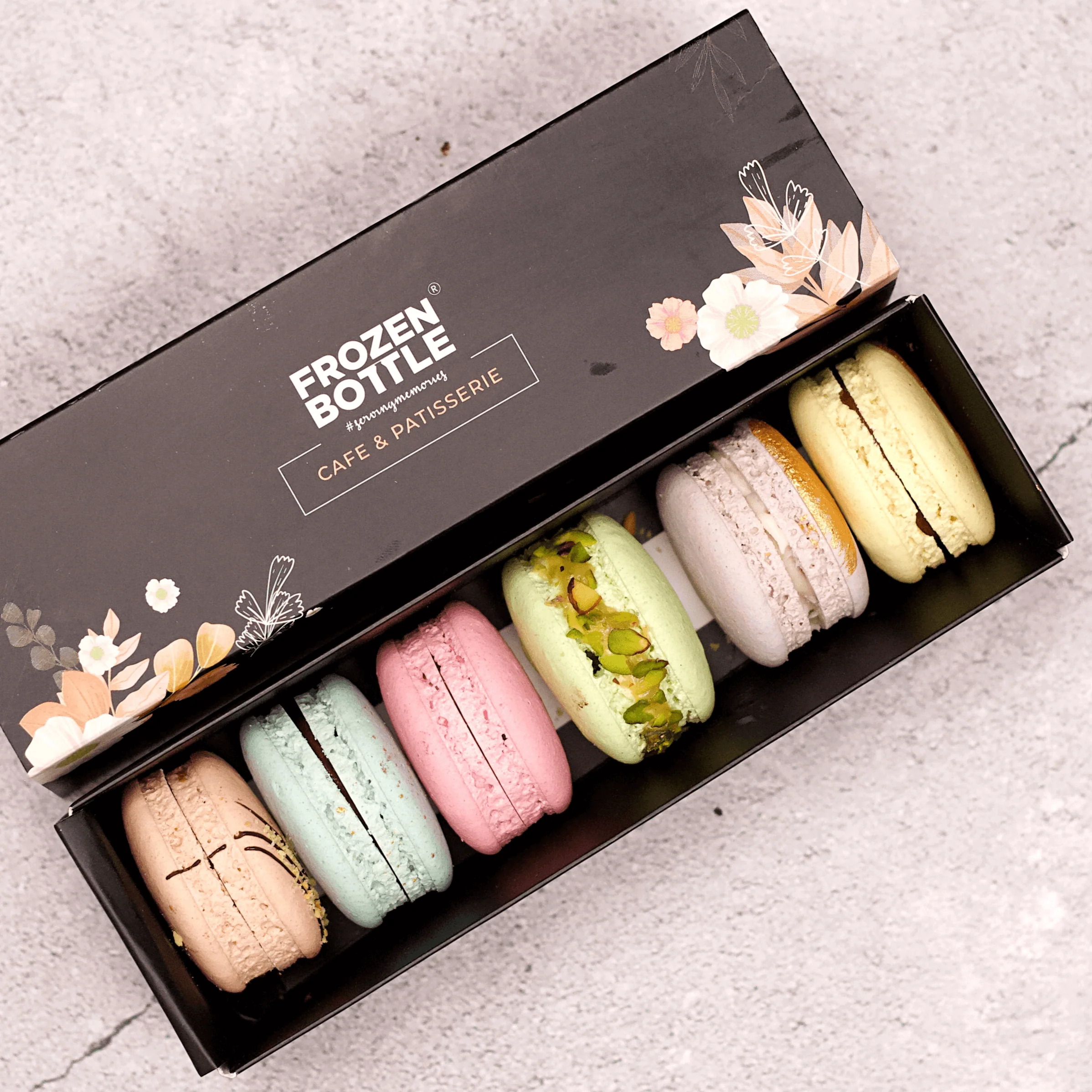 Black macaron box with colorful macarons and floral design, open view